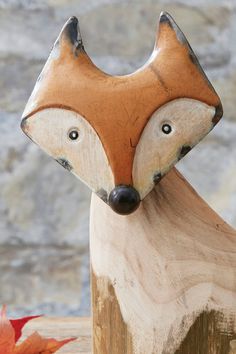 a wooden carving of a fox head on top of a tree stump next to leaves