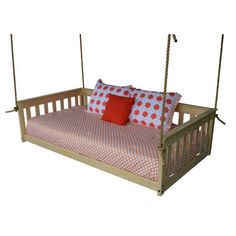 a bed with red and white pillows hanging from it's sides on a wooden frame