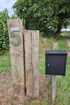 a mailbox and two wooden posts in the grass next to a dirt road with trees