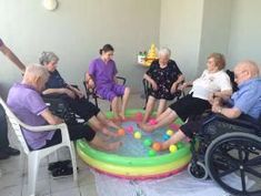 several elderly people sitting in chairs around an inflatable pool with balls on it