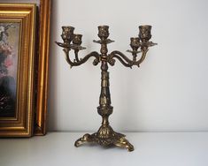 a gold candelabra with three candles on it in front of a painting