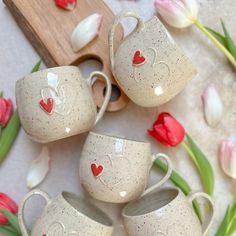 four coffee cups with hearts painted on them sitting next to tulips and a cutting board