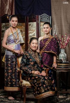 two women in traditional thai garb posing for a photo with one woman sitting on a chair