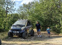 a man and his son are standing in front of a vehicle on a dirt road