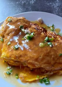 a white plate topped with food covered in gravy and green onion toppings