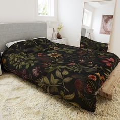 a bed with a black floral comforter on top of it next to a mirror