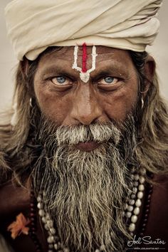 an old man with long white hair and blue eyes wearing a turban on his head