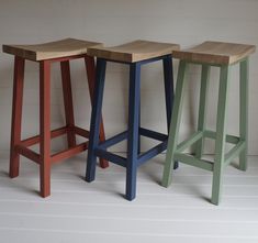 three different colored stools sitting next to each other on a white floor in front of a wall