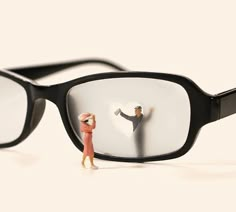 a miniature person standing next to a pair of glasses with the image of a man holding a woman's hand