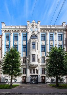 a large white building with blue windows and trees in front of it on a sunny day