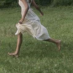 a woman in a white dress playing with a frisbee on a grassy field