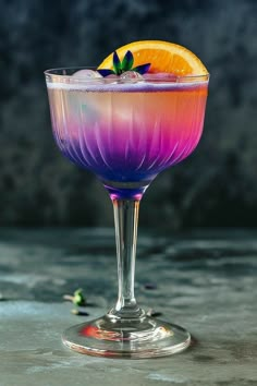 a purple and orange drink in a wine glass with a garnish on the rim