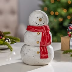 a snowman made out of ceramic sitting on a table next to a christmas tree