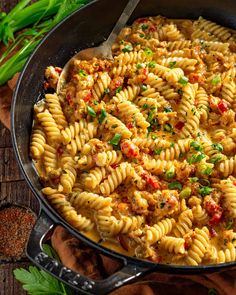 a skillet filled with pasta and sauce on top of a wooden table next to green onions