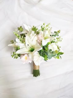 a bridal bouquet with white flowers and greenery on a bed sheet, top view