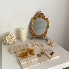 a white table topped with jewelry and a gold framed mirror on top of it's side