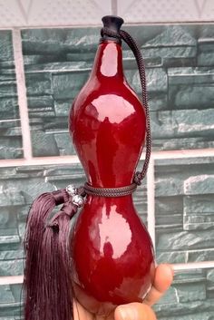 a hand holding a red glass bottle with a tassel