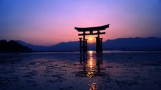 the sun is setting over an ocean with a floating gate in the foreground and mountains in the background