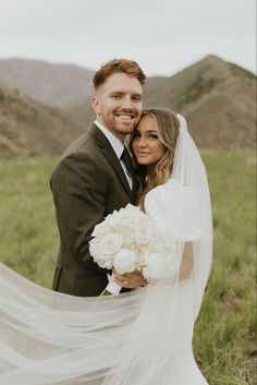 a bride and groom pose for a wedding photo in the mountains with their veil blowing in the wind