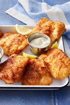 fried fish with lemon wedges and dipping sauce on a white plate next to a blue towel