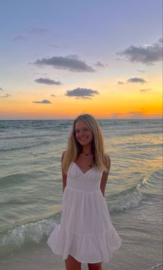 a woman standing on top of a sandy beach next to the ocean at sun set