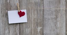 a piece of paper with a red heart pinned to it on a clothes line against a wooden wall