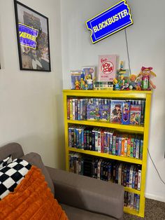 a yellow book shelf filled with books next to a gray couch and orange throw pillow