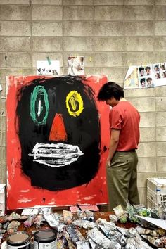 a man standing next to a large painting on top of a wooden table covered in paint