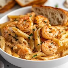 a white bowl filled with pasta and shrimp next to bread on a table, ready to be eaten