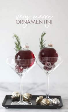 two wine glasses with ornaments in them sitting on a tray that says very merry ornamentii