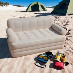 an inflatable couch and sunglasses are on the sand next to two camping tents