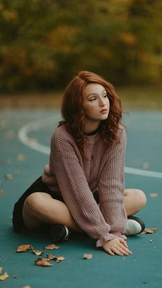 a woman is sitting on the ground with her hands in her pockets and looking off into the distance