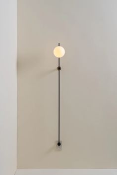 a white wall with a black pole and a light on it's side in the corner