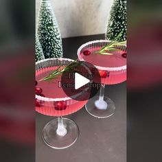 two cocktails with cranberry and rosemary garnish sit on a table