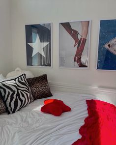 a bed with red pillows and pictures on the wall above it, along with other decorative items