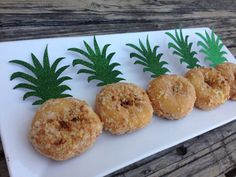 three donuts with pineapples on them sitting on a white platter next to green leaves