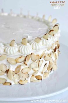 a cake with white frosting and almonds on top is sitting on a plate