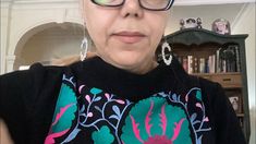 an older woman wearing glasses and a black shirt with colorful flowers on the front is looking at the camera