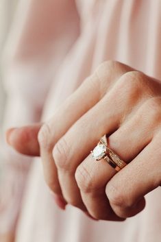 a woman's hand wearing a gold ring with a white diamond on the middle