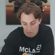 a man sitting at a table with a hot dog in his hand and looking down