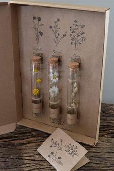 three glass bottles filled with sand and flowers on top of a wooden table next to a card