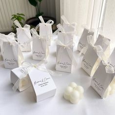 small white boxes with tags on them sitting on a table next to candles and flowers