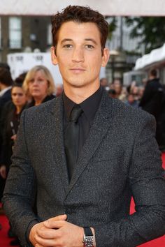 a man in a suit and tie standing on a red carpet with people behind him