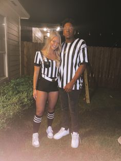 a man and woman dressed up in referee outfits standing next to each other outside at night