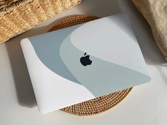 an apple laptop sitting on top of a table next to a wicker basket and pillow