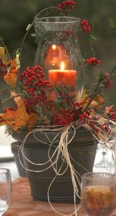 a candle is lit on top of a potted plant with autumn leaves and berries