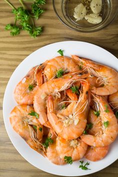 a white plate topped with cooked shrimp and garnished with parsley on the side