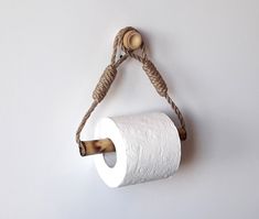 a roll of toilet paper hanging from a rope on the wall with a wooden handle