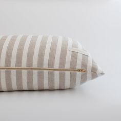 a white and grey striped pillow with gold zipper on the front, sitting on a white surface