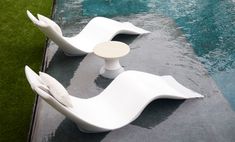 two white chairs sitting next to each other near a swimming pool with grass in the background